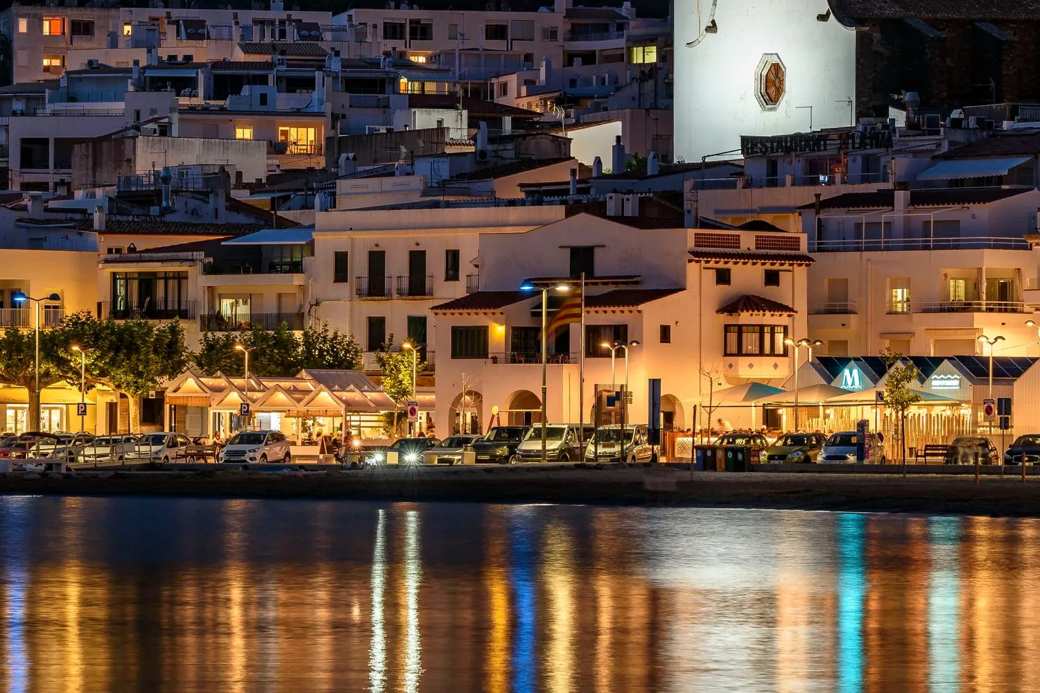 El front marítim del Port de la Selva de nit, amb els llums reflectits a l'aigua